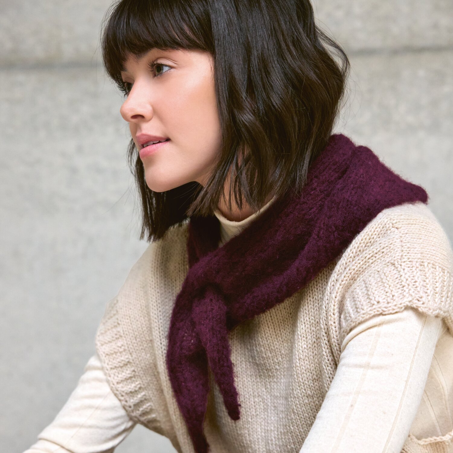 Strickset Dreieckstuch Modell 04 aus Luxury Knits - Premium Natural Fibres von Rico Design Strickset Dreieckstuch Modell 04, weinrot, aus Luxury Knits. Frau trägt das Tuch über einem cremefarbenen Pullover.