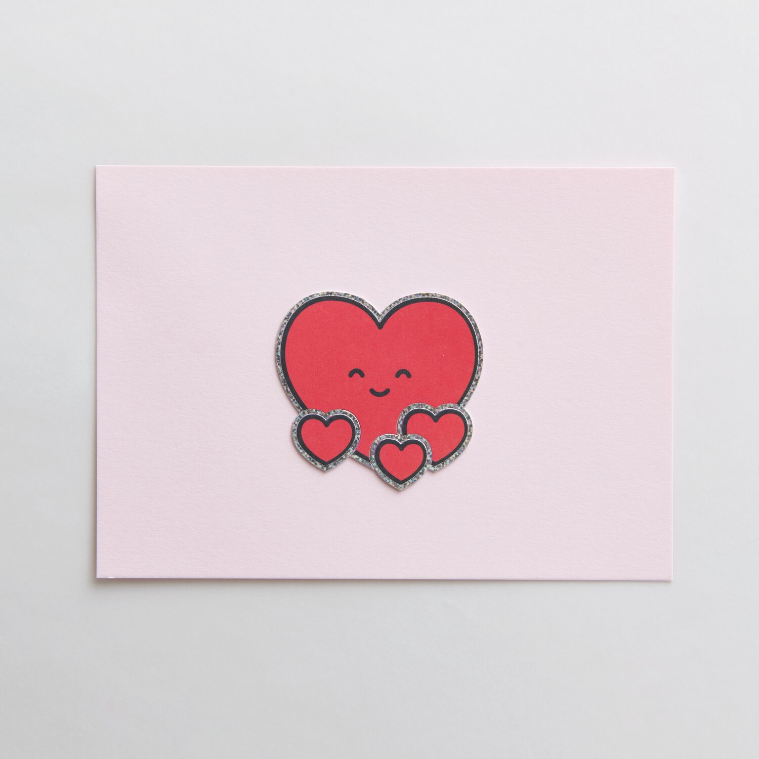 Paper Poetry Clip-Ons Chingu Herzen Rot: Rote Herz-Clips mit lächelndem Gesicht auf rosa Hintergrund.