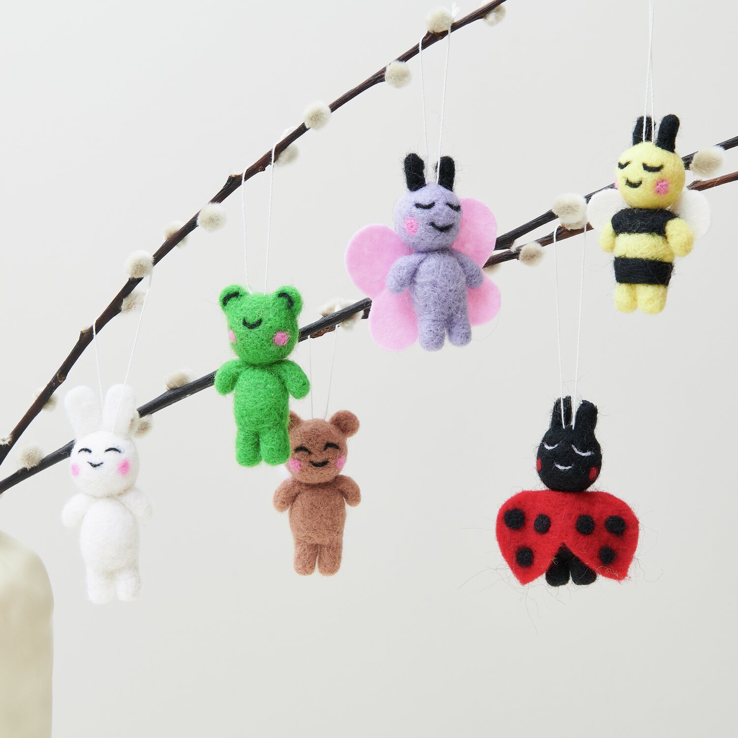 Aufhänger Filz-Hase 3D: Weißer Filzhase an Zweig. Weitere Figuren: Bär, Schwein, Frosch, Biene, Marienkäfer.