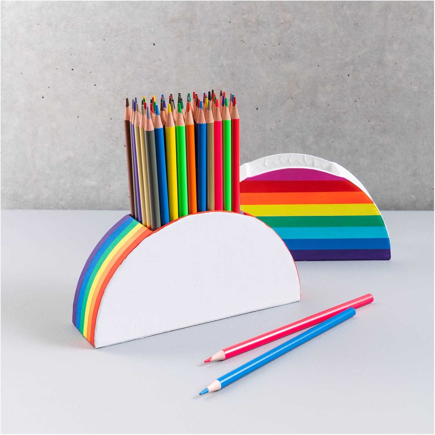 Stiftehalter aus Pappe halbrund 18x9x5cm Farbe Weiß von Rico Design Stiftehalter aus Pappe halbrund mit Regenbogenmuster, gefüllt mit bunten Buntstiften, von Rico Design.