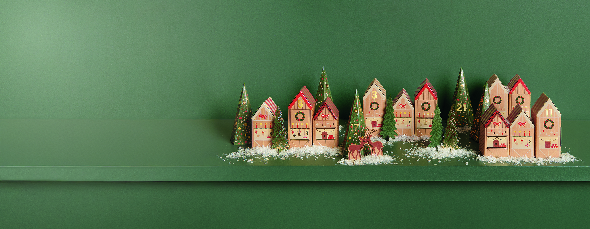 Papphäuser und Papptannen stehen dekoriert vor einem grünen Hintergrund