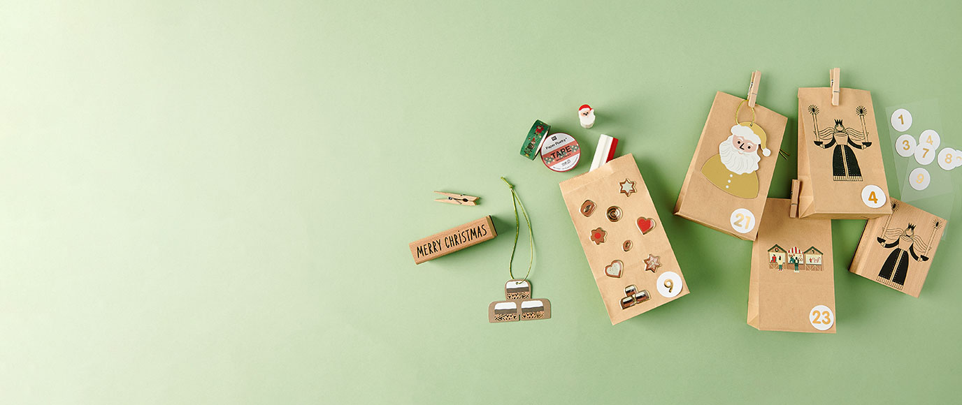 Blockbodenbeutel mit weihnachtlichen Stickern verziert, daneben Stempel, Geschenkanhänger und Washi Tape. Flatlay von Produkten.