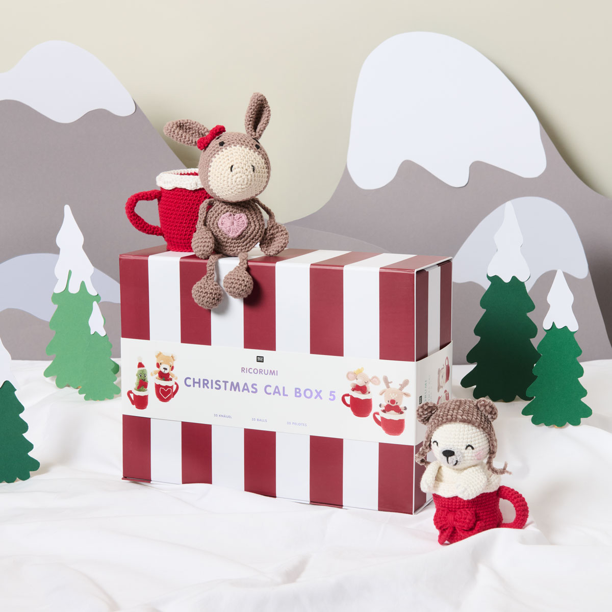 Eine Christmas CAL Box 5 mit zwei dazugehörigen gehäkelten Figuren und Tassen. Fotosetting gebastelte Winter-Berglandschaft.