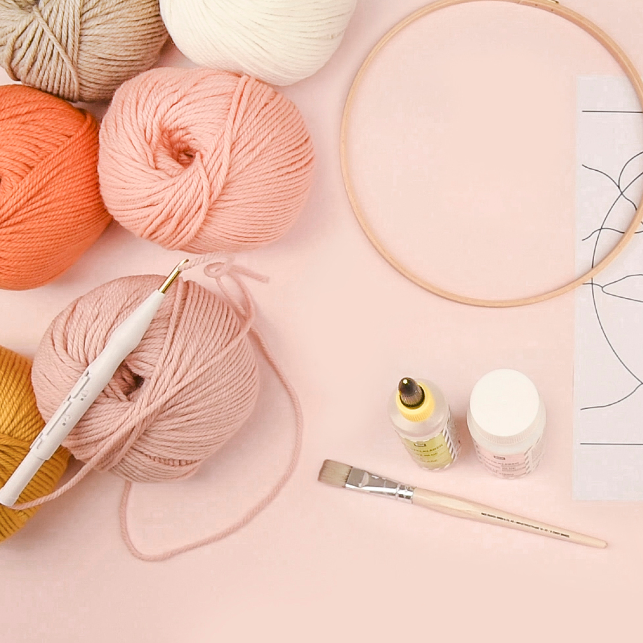 Punch Needle, Stickrahmen, Stickvorlage, Wollknäuel in Rosatönen und weiteres Punch Needle Zubehör liegen auf rosa Hintergrund