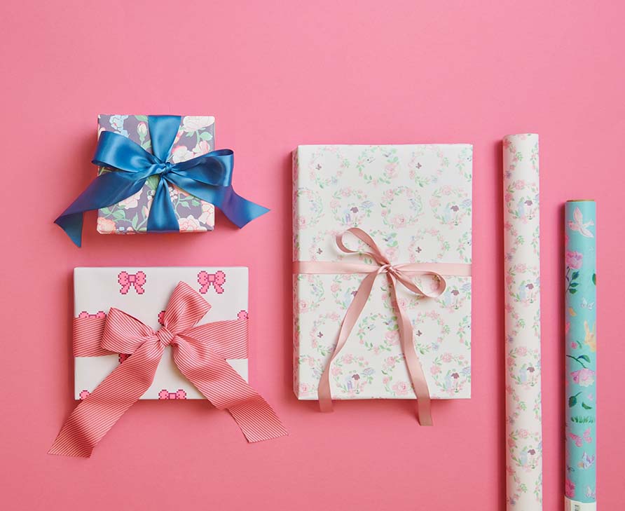 Drei verpackte Geschenke mit Schleife neben zwei Geschenkpapierrollen. Flatlay von Produkten.