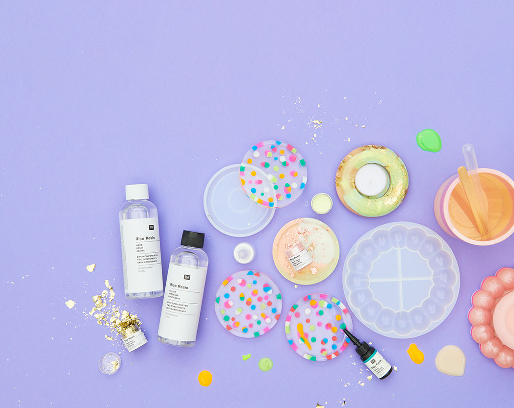 Drei bunte Glasuntersetzer und ein Teelichthalter aus Resin gegossen, dazu das passende und nötige Material. Flatlay von produkten.