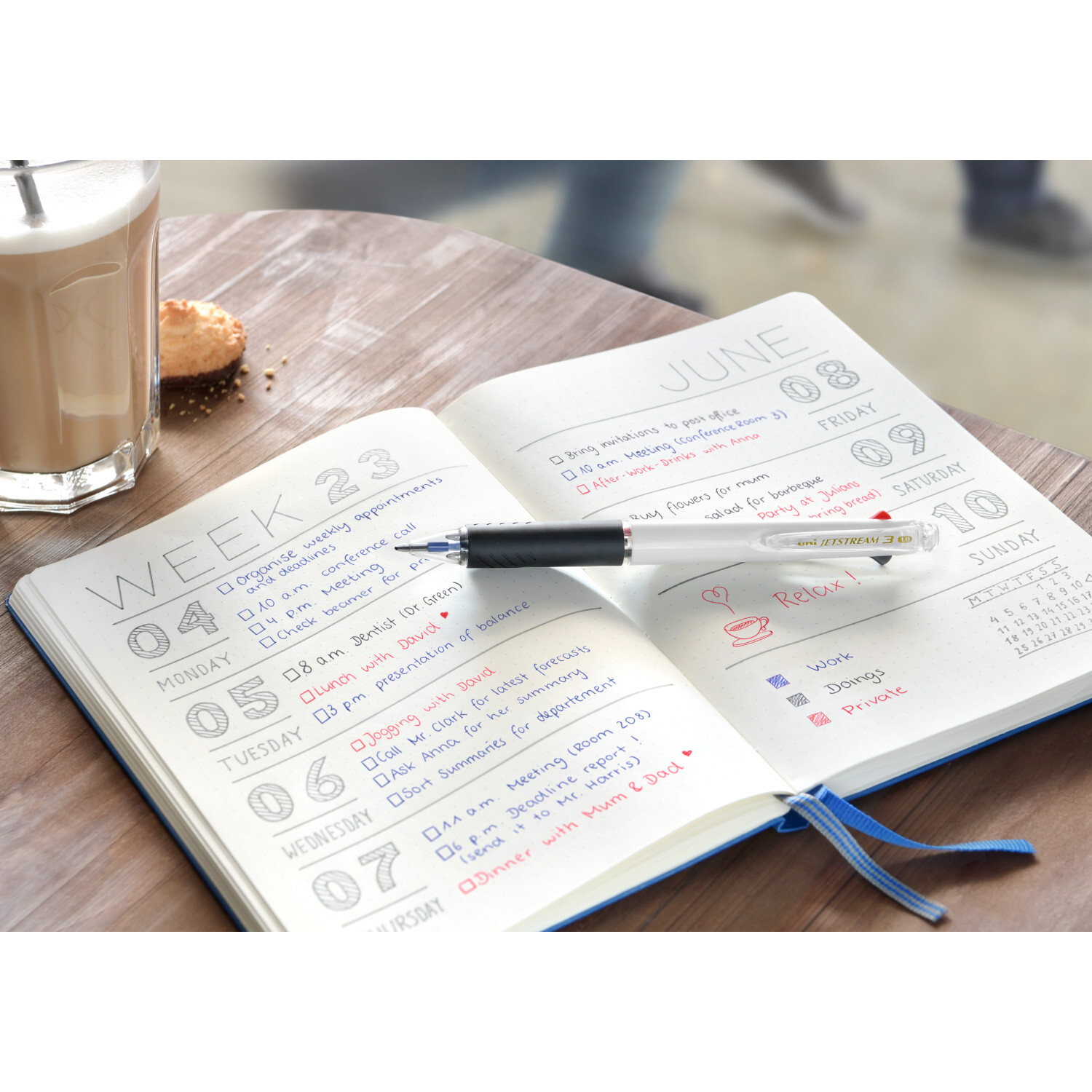 Tintenroller uni-ball Jetstream liegt auf einem geöffneten Kalender mit blauer und roter Schrift.