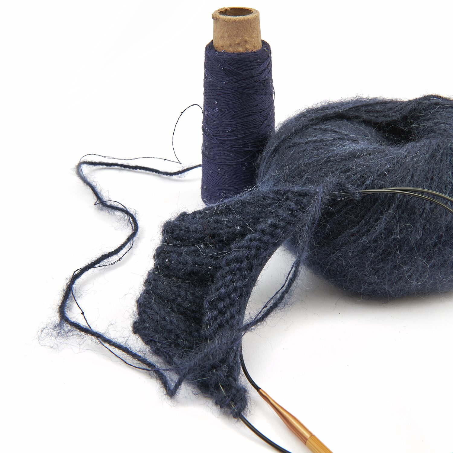 Lovewool No. 21 Herbst-Winter Sprachauswahl deutsch von Rico Design Dunkelblaues Strickgarn und Strickstück mit Stricknadeln, daneben eine Garnrolle. Ideal für kreative Strickprojekte. Perfekt für Handarbeitsliebhaber.