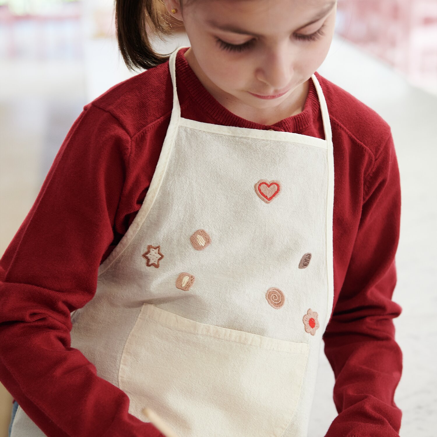 Stick & Stitch Stickpackung Kekse 23 Stück: Mädchen in rotem Pullover mit bestickter Schürze.