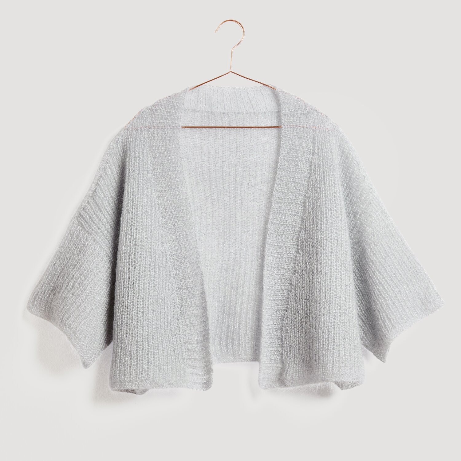 Lovewool No. 21 Herbst-Winter Sprachauswahl deutsch von Rico Design Grauer Strick-Cardigan von Modell Legeware, präsentiert auf einem Kleiderbügel. Der weiche Stoff und das offene Design machen ihn ideal für kühle Tage. Perfekt für einen lässigen, stilvollen Look.