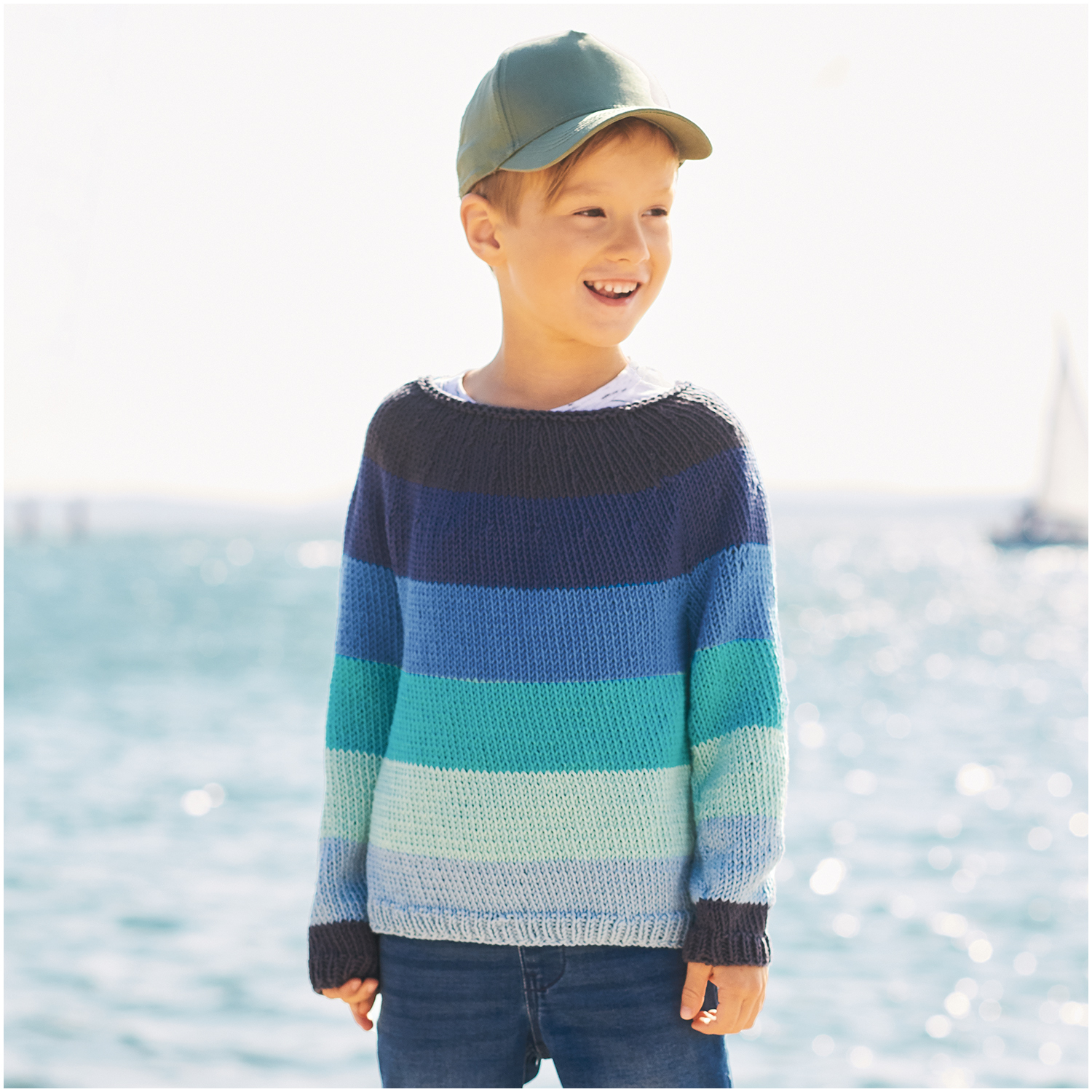 Essentials Organic Cotton aran: Junge am Meer in gestreiftem Pullover in Blautönen, Marke Rico Design.