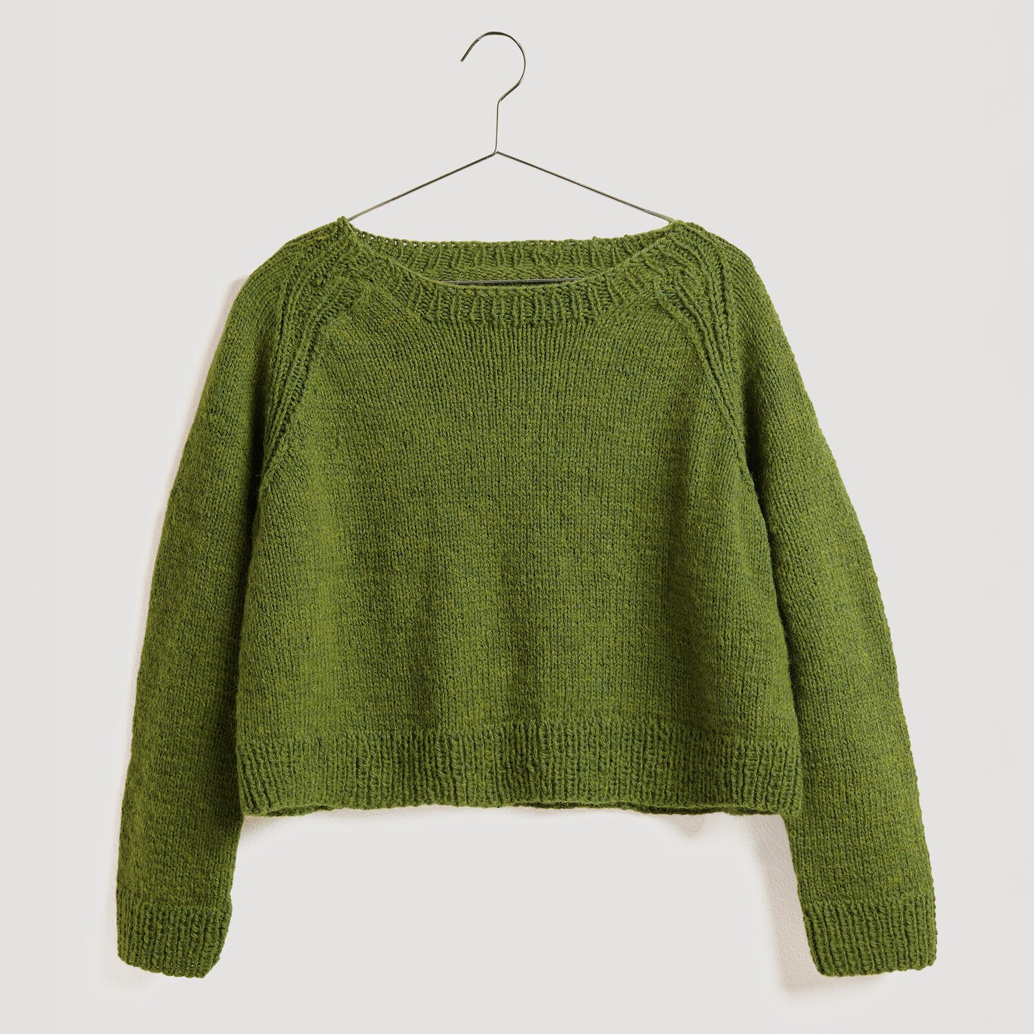 Die Neue Masche No. 13 Herbst von idee. Creativmarkt Strickset Pullover Modell 20 aus Die Neue Masche No. 13, olivgrün, aus Soft Alpaca, hängt an einem Kleiderbügel.