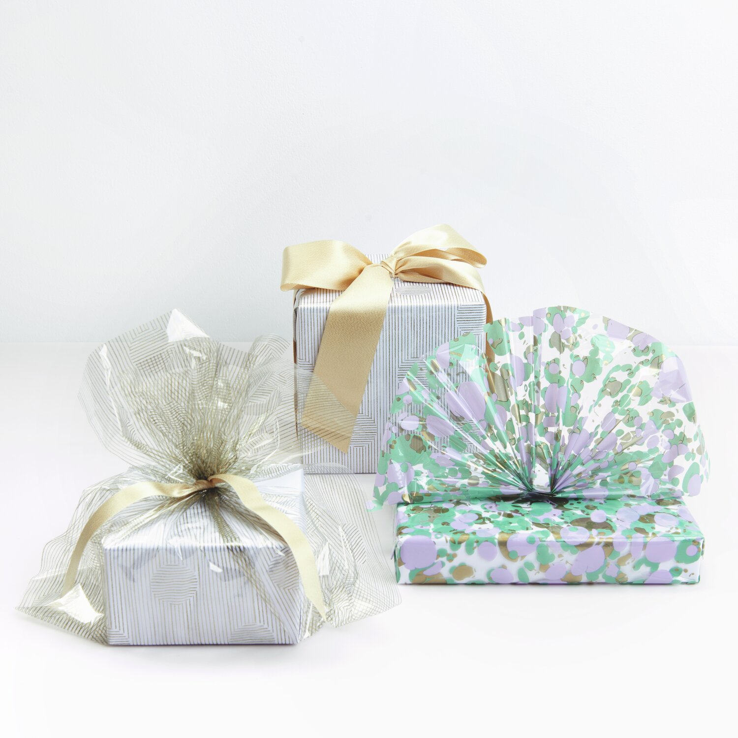 Paper Poetry Geschenkfolie Mix The Sky is the Limit: Drei elegant verpackte Geschenke mit goldenen Schleifen und gemustertem Papier.