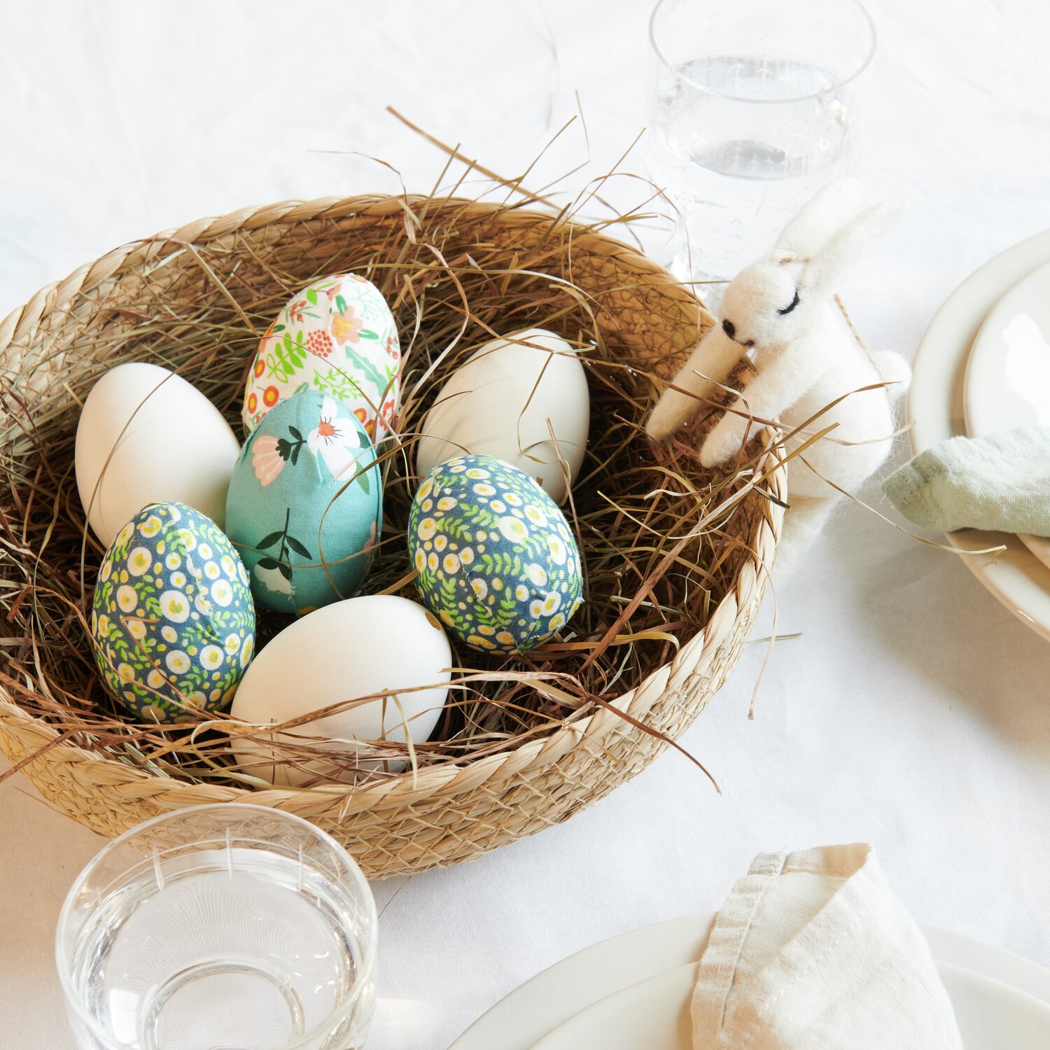 Korb geflochten mit bunten Ostereiern und einem Stoffhasen auf einem gedeckten Tisch. Ideal für Osterdekoration.