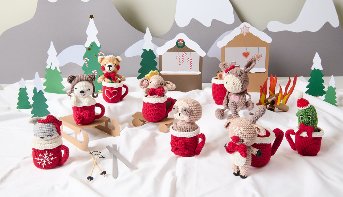 Häkelanleitung Ricorumi CAL Ava the Arctic Fox Häkelanleitung Ricorumi CAL Ava the Arctic Fox: Niedliche Amigurumi-Tiere in roten Tassen vor winterlicher Kulisse.