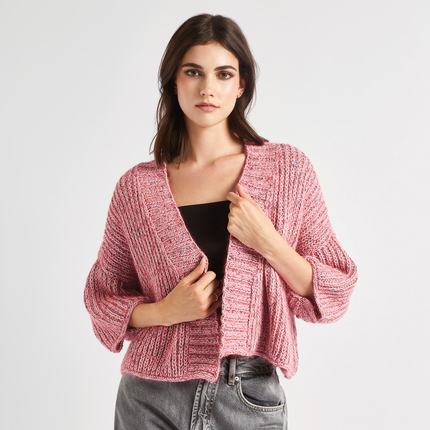 Strickanleitung Kimono-Jacke mit Beilaufgarn: Frau trägt rosa Strickjacke über schwarzem Top.