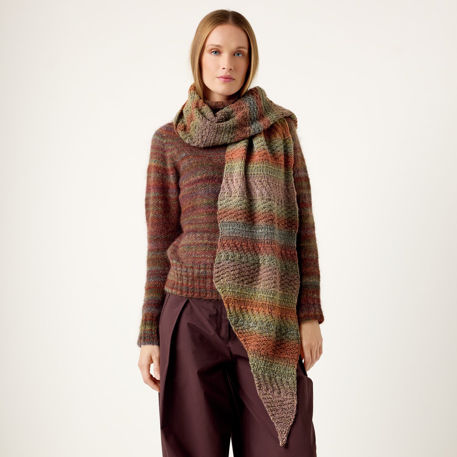 Strickset Tuch Modell 19 aus Die Neue Masche No. 13 von idee. Creativmarkt Strickset Tuch Modell 19: Frau trägt gestrickten Schal in Erdtönen, kombiniert mit braunem Pullover und Hose.