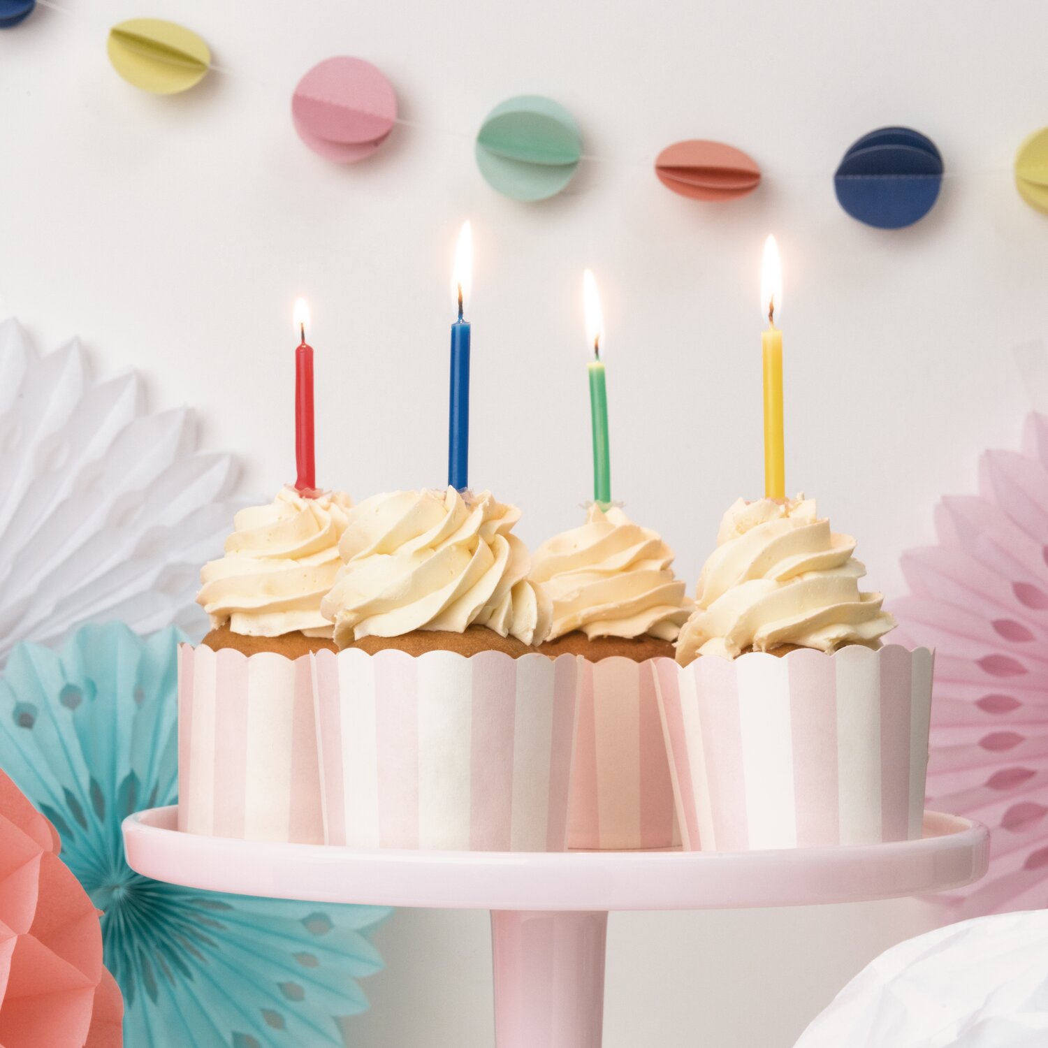 Kerzenset Basic mit 48-teiligem Zubehör von Rico Design auf Cupcakes, dekoriert mit verschiedenfarbigen Kerzen vor festlicher Partydeko