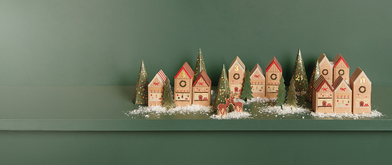 Papphäuser und Papptannen stehen dekoriert vor einem grünen Hintergrund