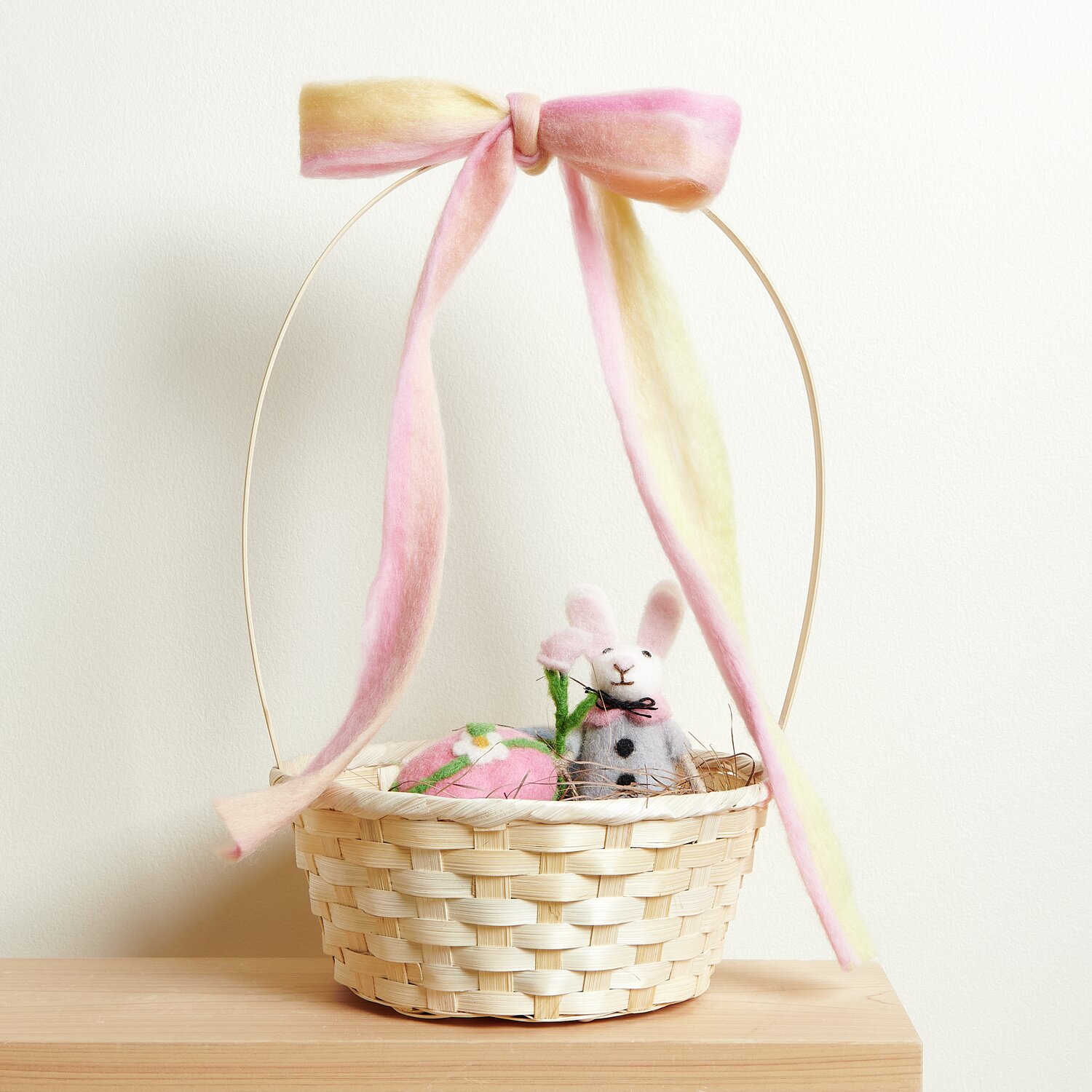 Aufhänger Filz-Hase mit Jacke und Blume in weißem Bambus Korb mit Henkel, dekoriert mit rosa Schleife.