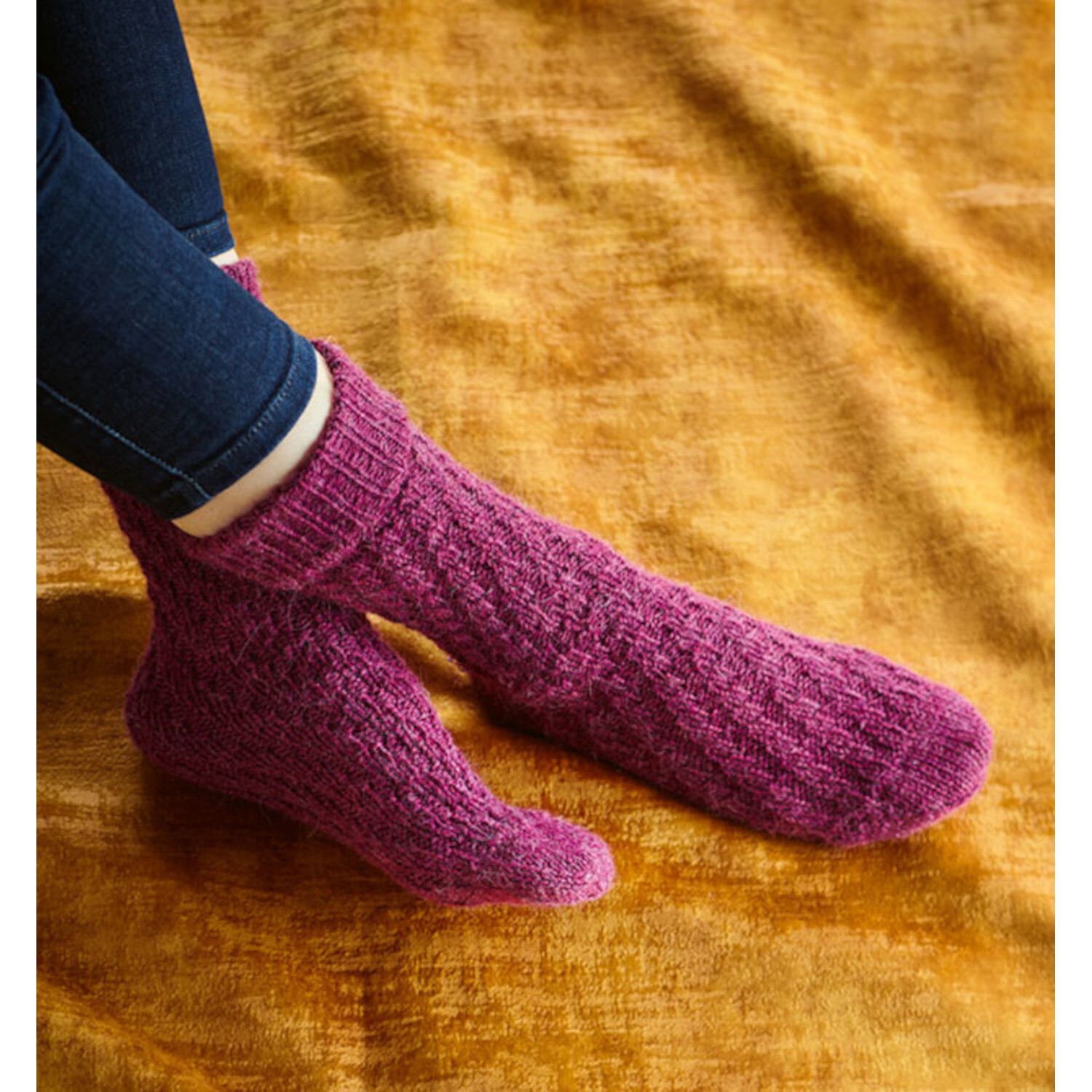 Tube Socks stricken: Lila gestrickte Socken auf goldenem Stoff, getragen von Person in Jeans.