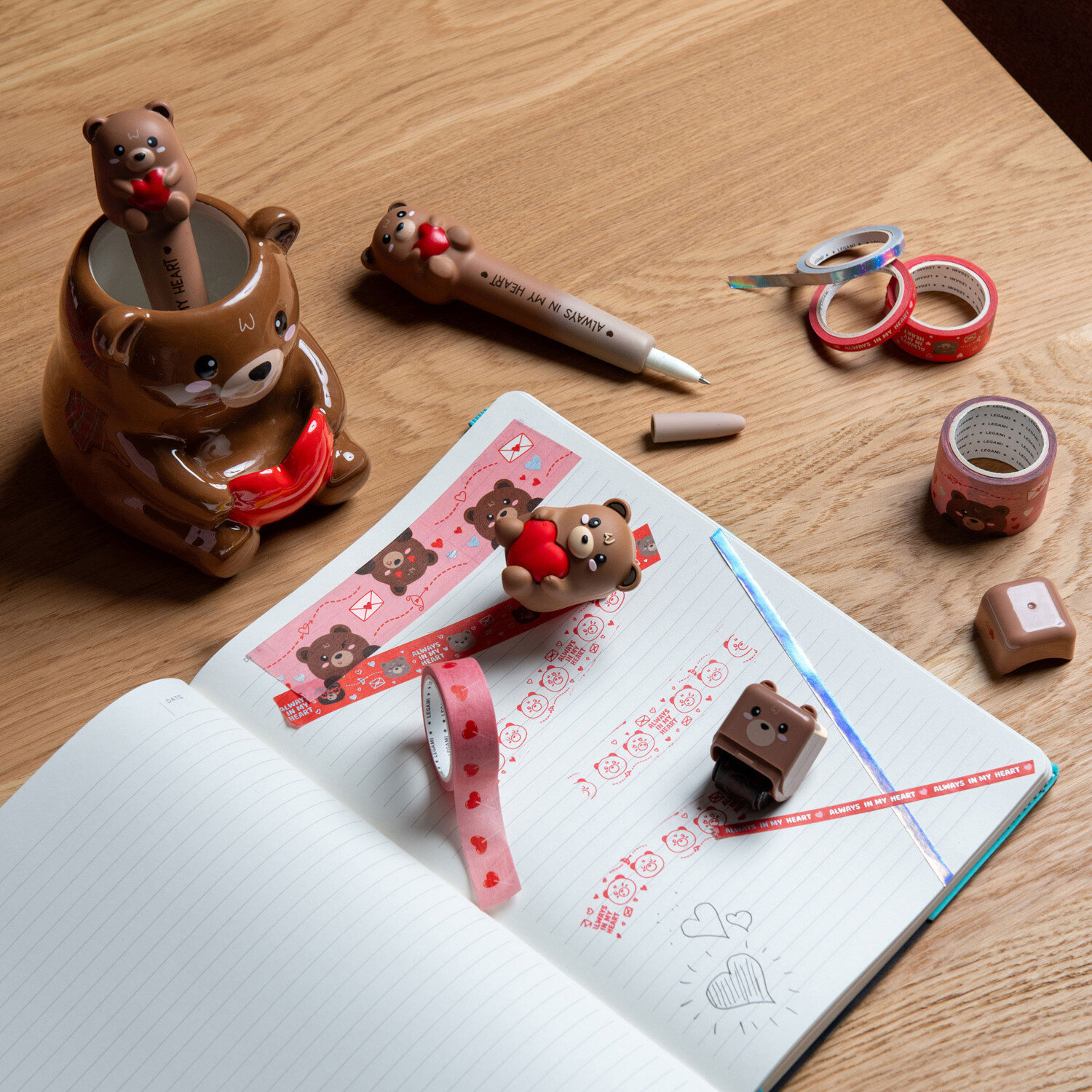 Deco Roller Stempel von Legami, braunes Bärchen-Motiv auf dekorativen Klebestreifen, arrangiert mit passendem Stiftehalter und geöffnetem Notizbuch auf Holztisch