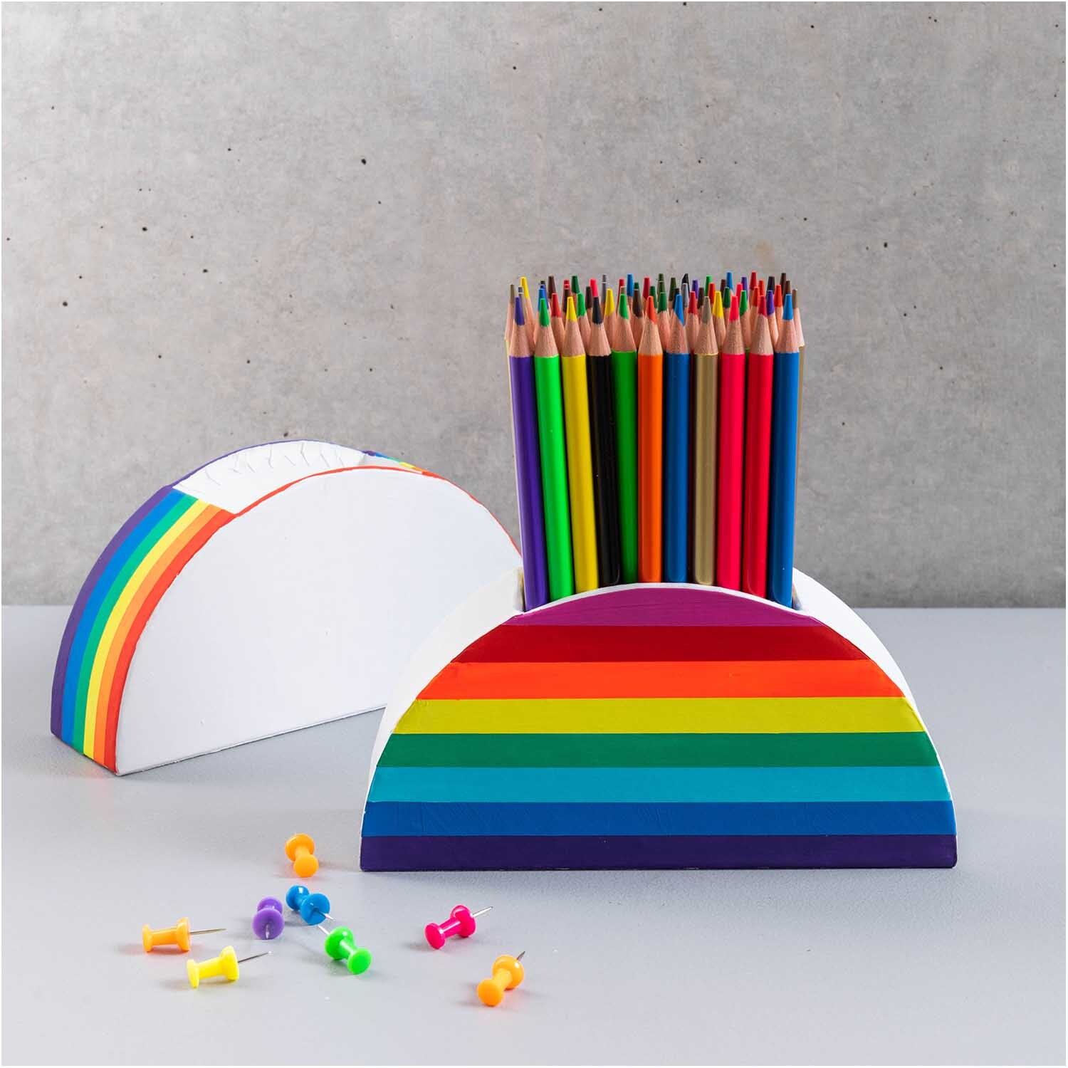 Stiftehalter aus Pappe halbrund 18x9x5cm Farbe Weiß von Rico Design Stiftehalter aus Pappe in halbrunder Form mit Regenbogenstreifen, gefüllt mit bunten Stiften.