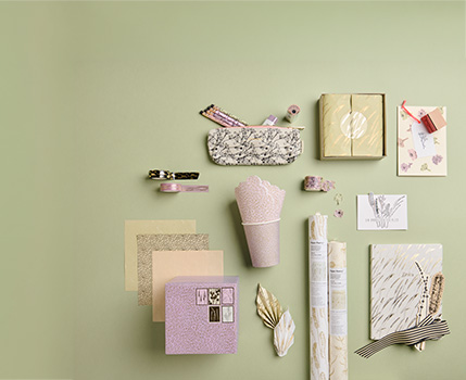 Flach ausgelegte Papeterie- und Geschenkartikel in Pastellfarben auf hellgrünem Hintergrund, darunter Notizbuch, Geschenkverpackungen, Karten, Geschenkpapier und dekorative Accessoires.