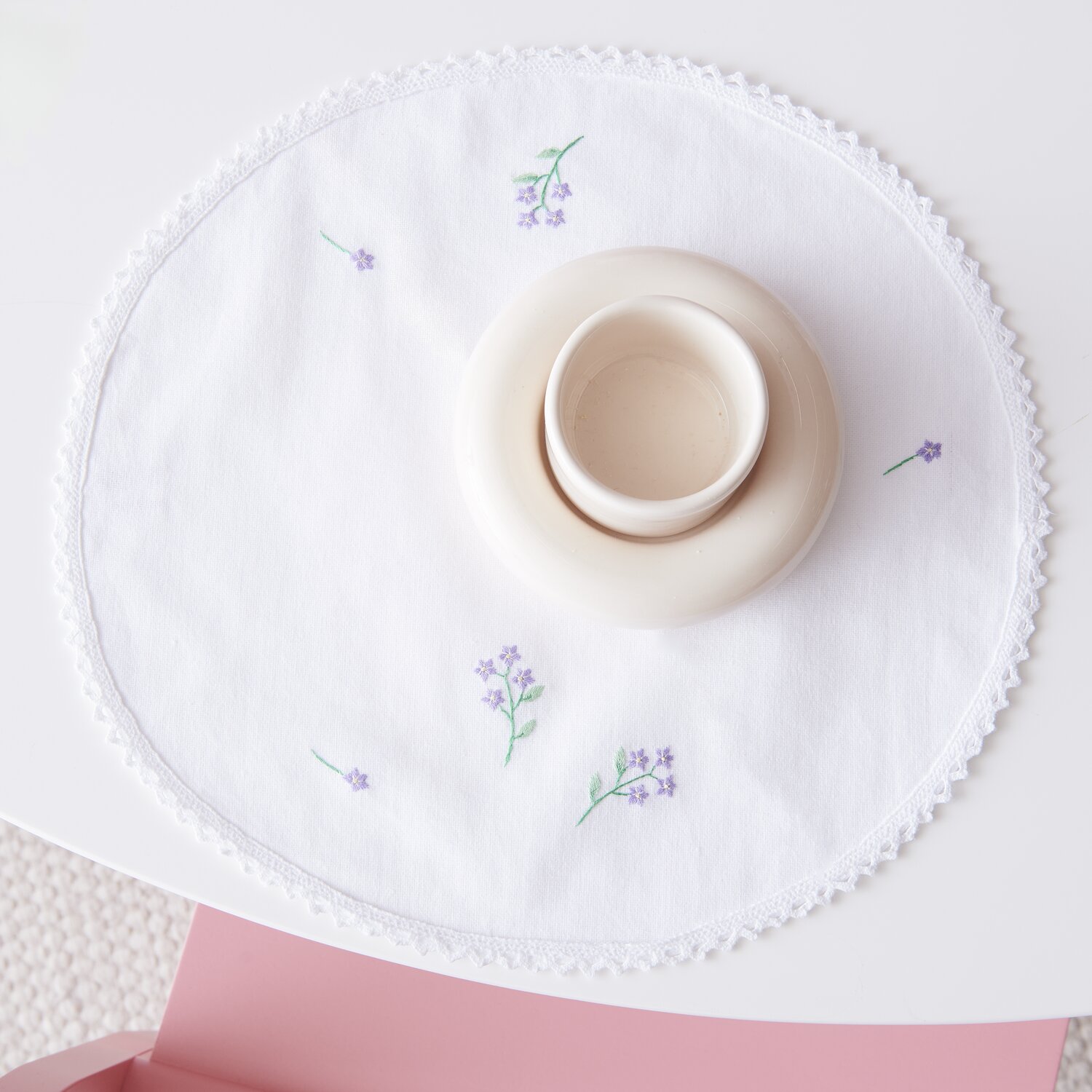 Stick & Stitch Packung Blumenkränze XL 13 Stück: Weißes Deckchen mit lila Blumenstickerei, dekoriert mit einer beigen Tasse auf rosa Tisch.