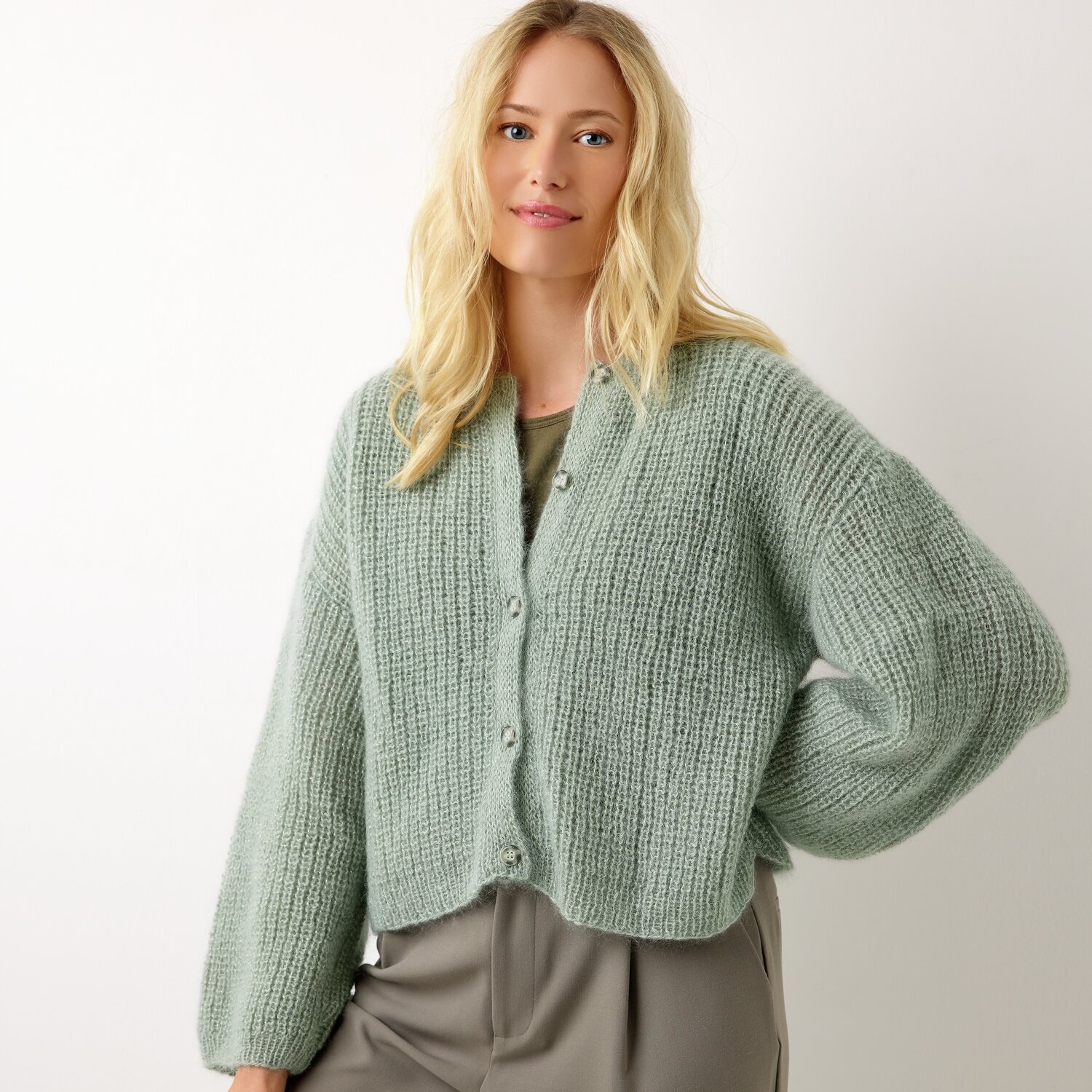 Strickset Kimono-Jacke Modell 24 aus Die Neue Masche No. 13 von idee. Creativmarkt Strickset Kimono-Jacke Modell 24 aus Die Neue Masche No. 13 in sanftem Grün, getragen von einer Frau vor weißem Hintergrund.