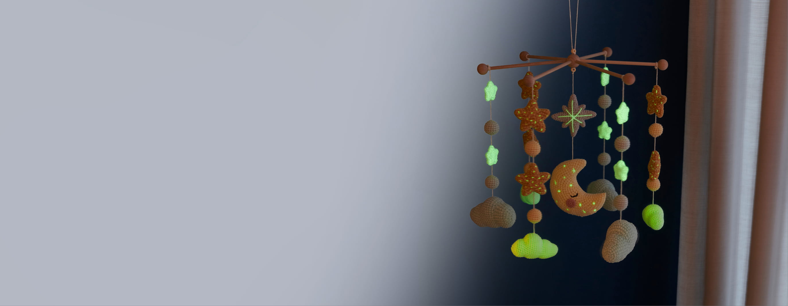 Mobile mit gehäkelten Sternen, Wolken, Kugeln und Mond hängt in einem dunklen Raum