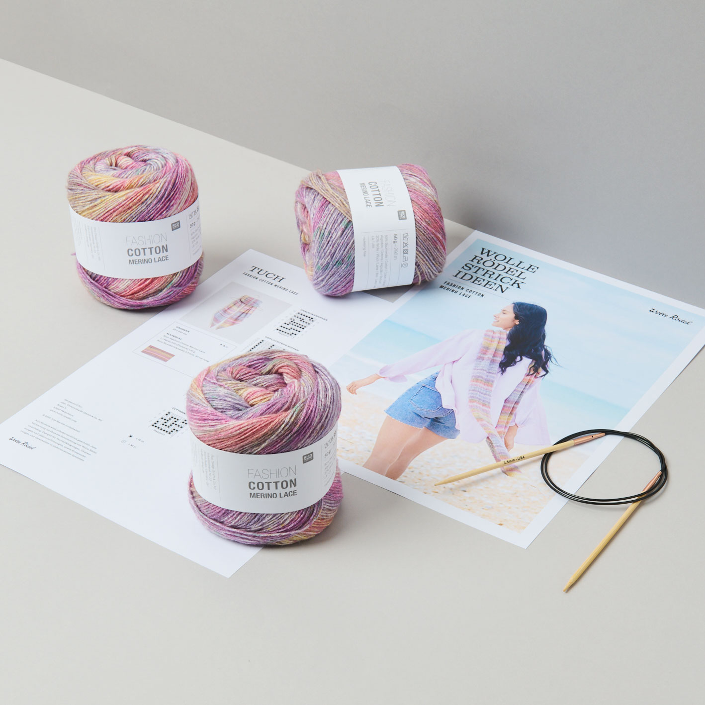 Drei Wollknäul und Stricknadel liegen auf einer Anleitung. Fotosetting graue Ecke.