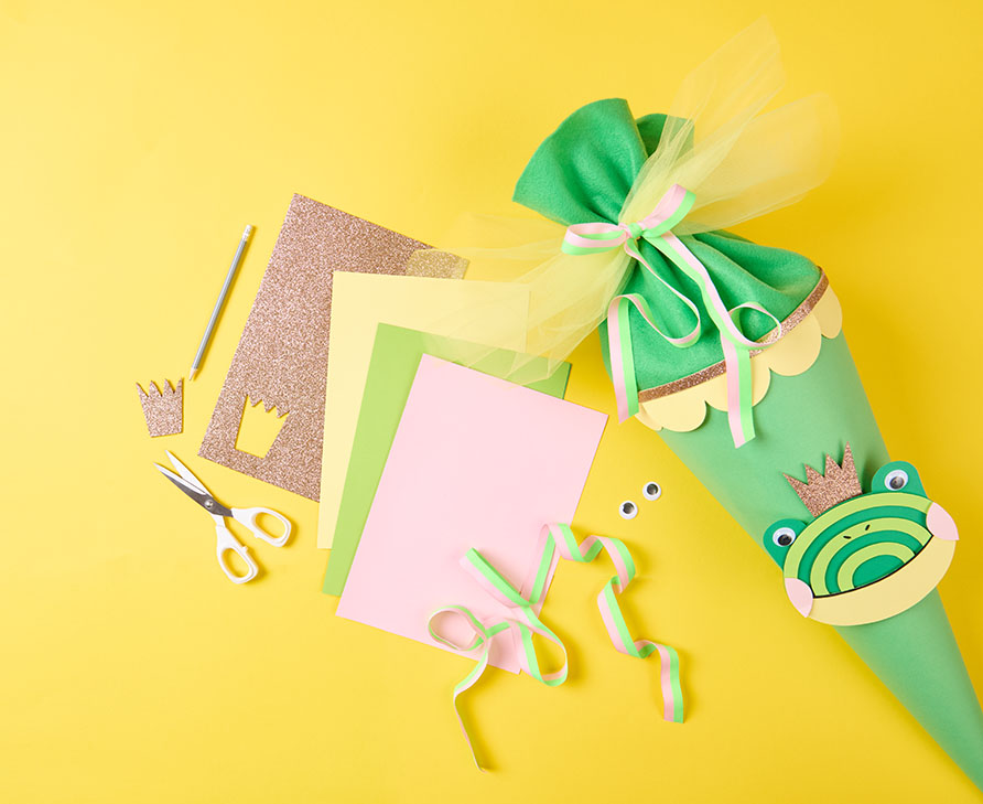 Grüne Schultüte neben Papier und Bastelmaterial. Flatlay von Produkten.