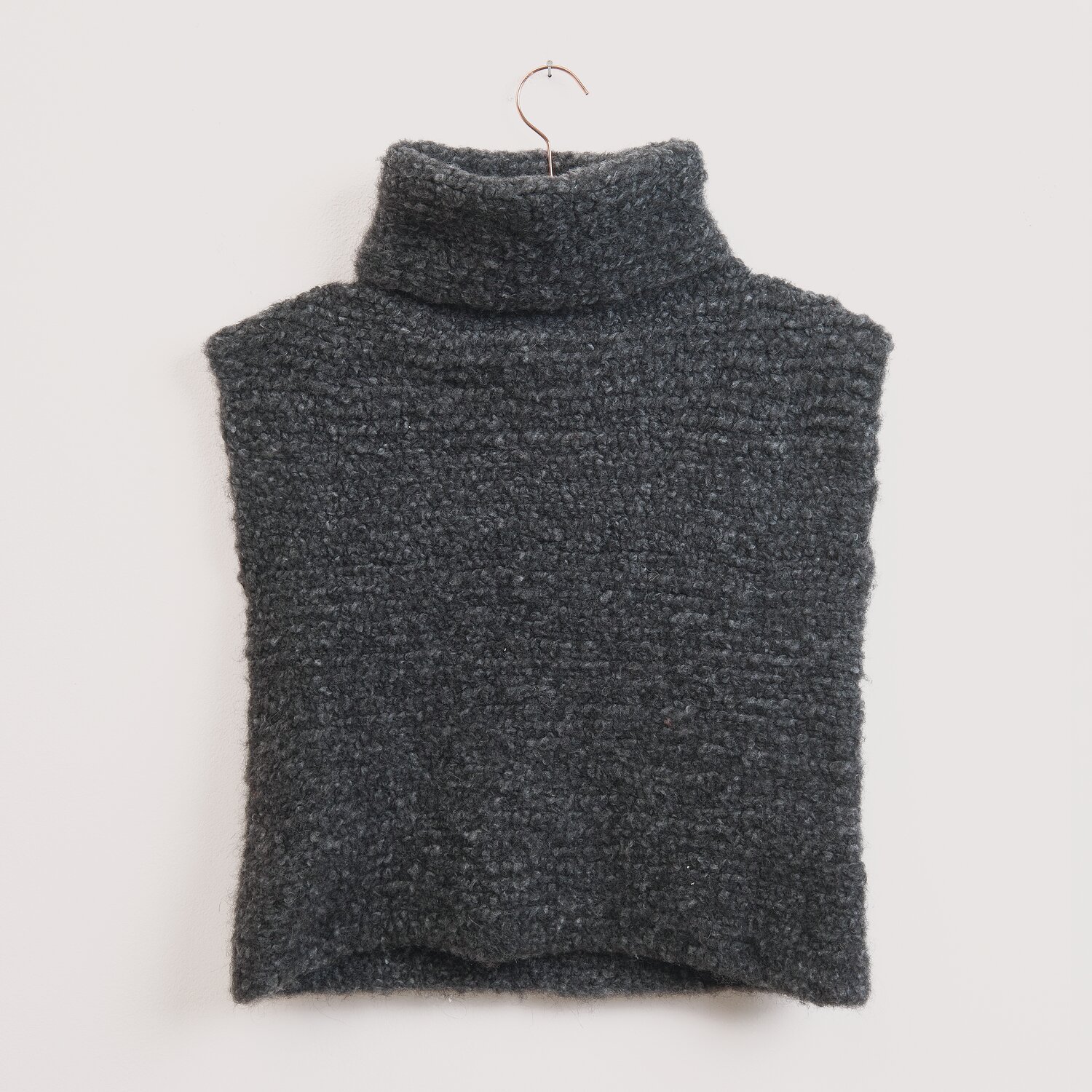 Die Neue Masche No. 16 Herbst, gestrickter Rollkragenponcho von Wolle Rödel in dunklem Melange-Grau, locker fallend an weißer Wand auf Bügel präsentiert.