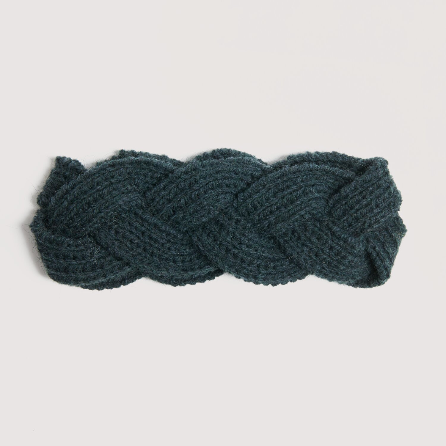 Strickset Stirnband Modell 16a aus Die Neue Masche No. 16 zeigt ein geflochtenes Wolle Rödel Stirnband in dunklem Ton, quer auf hellem Hintergrund platziert