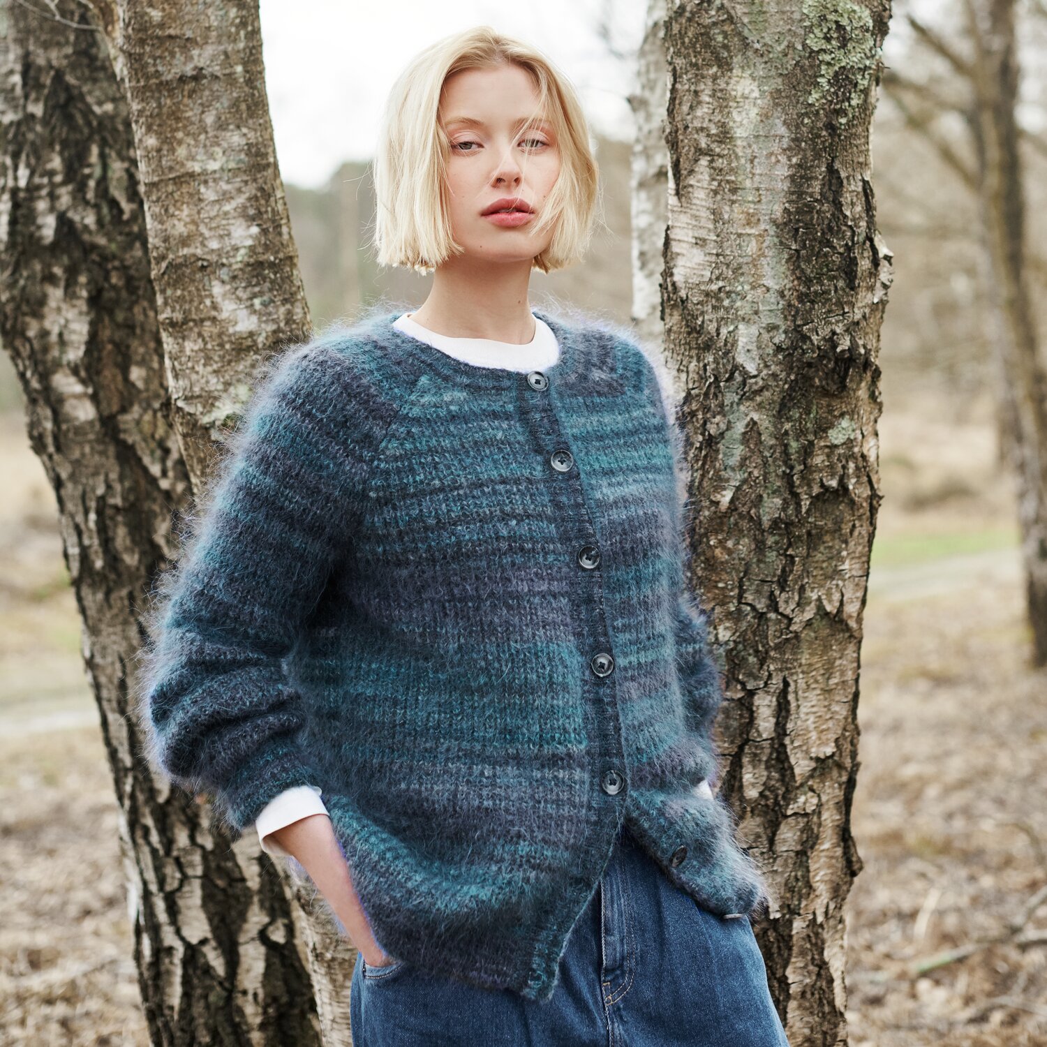 Strickset Cardigan Modell 26 aus Lovewool No. 21 von Rico Design Strickset Cardigan Modell 26 aus Lovewool No. 21: Frau trägt blauen Cardigan im Wald.