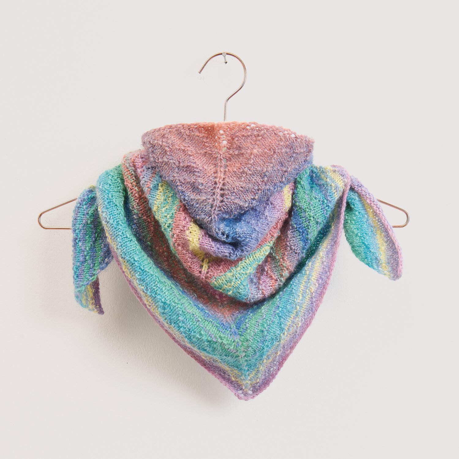 Die Neue Masche No. 16 Herbst, gestricktes Dreieckstuch von Wolle Rödel mit weichem Farbverlauf in Pastelltönen, dekorativ auf einem Bügel präsentiert