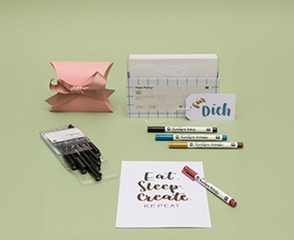 Weiße Karten in der Verpackung, eine Geschenkschachtel, eine beschriftete Karte und Geschenkanhänger mit Brushpens und verpackten Pigment Linern.